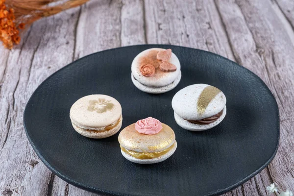 Four macarons, decorated with edible ink and fondant, on a black plate.