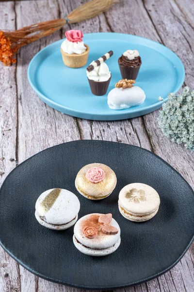Macarons decorated with edible ink and fondant. In the background assorted sweets with whipped cream and nuts.