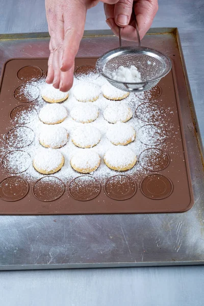 Confectioner sprinkling sugar over wedding sweet treats on a brown silicone plate_vertical.