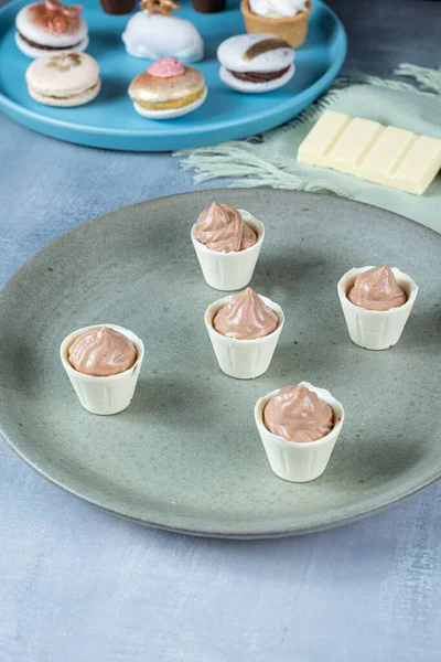 Small white chocolate cups filled with chocolate cream on a green plate.