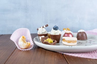 Small chocolate cup topped with whipped cream and blueberries next to other fancy sweets_side view.