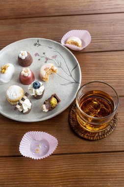 Small chocolate glass with bitten pistachio cream, next to macaron, truffles, walnut cameo and whiskey glass_vertical.