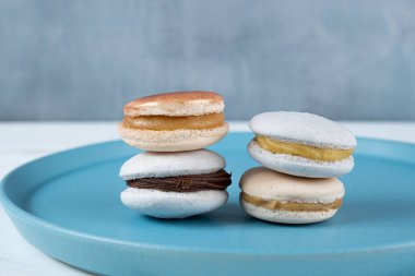 Close Up of macarons with chocolate ganache filling and dulce de leche stacked on a blue plate.