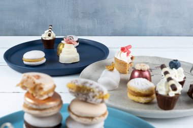 Small white chocolate cake next to assorted sweets. In the blurred foreground, macarons stacked.