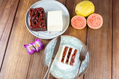 Slices of guava sweet and curd cheese next to a copper knife and fork_top view.