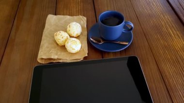Three Brazilian cheese breads next to a cup of coffee with smoke and tablet.