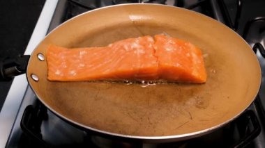 Salmon fillet with garlic on top, being done in the skillet with butter.