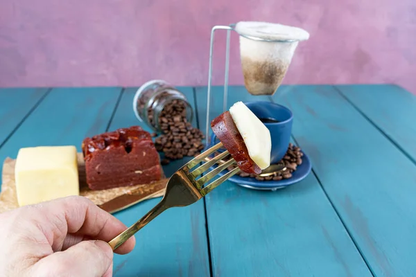 Elinde çatal ve peynirli guava tatlısı tutan bir adam. Bulanık arka planda fasulye ve kahve fincanı var..