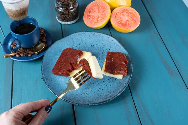 Elinde çatal ve peynirli guava parçaları olan bir kadın. Etrafı fasulye ve kahve dolu..