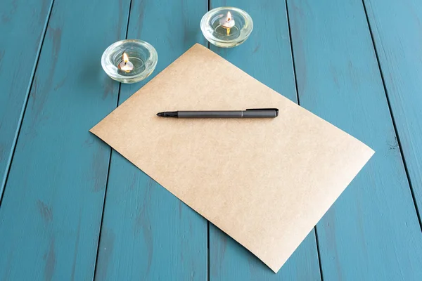 Kahverengi kağıdın üzerindeki gri dolmakalem, yanan mumların yanında..