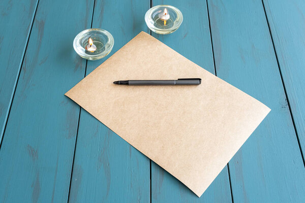 Gray fountain pen on brown paper, next to lit candles.