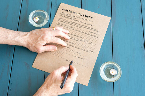 Man's hands with fountain pen signing contract next to lit candles.