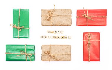 Mutlu Noeller. Tahta küplerden yapılmış mesaj. Beyaz, düz bir yatakta hediye kutuları. Kış tatili tebrik kartı, davetiye ya da broşür.