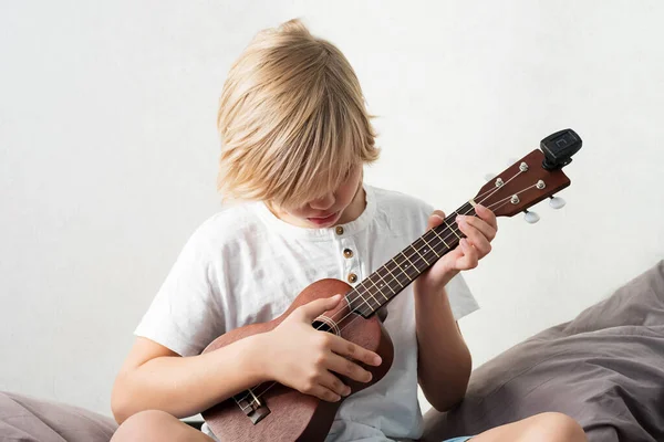 Young Boy Tuning Ukulele Home Blond Haired Boy Sitting Couch — Stock Photo, Image