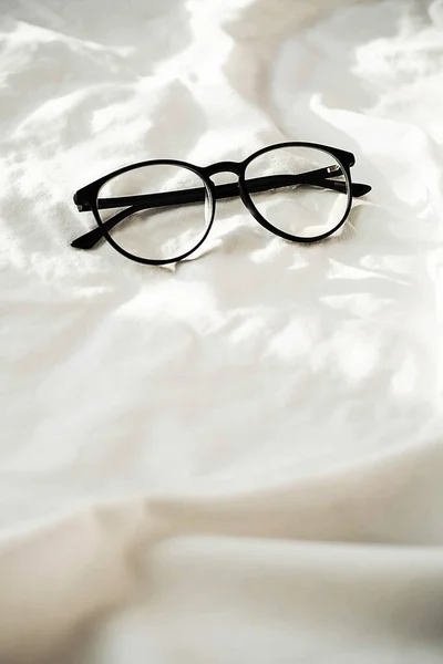 Stylish Eyeglasses White Bedding Sunlight Shadows Flat Lay Fashion Accessories — Stock Photo, Image