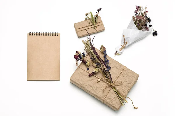 Hediye kutuları sarılı el işi kağıtlar, dekore edilmiş doğal kurumuş çiçekler, boş spiral defter, düz yatak. Sıfır atık tatil hediye paketi. Kadınlar günü, anneler günü ya da paskalya kutlaması konsepti. 