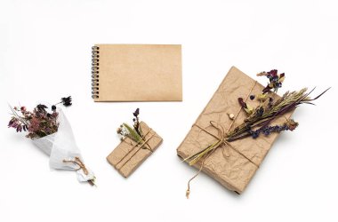 Hediye kutuları sarılı el işi kağıtlar, dekore edilmiş doğal kurumuş çiçekler, boş spiral defter, düz yatak. Sıfır atık tatil hediye paketi. Kadınlar günü, anneler günü ya da paskalya kutlaması konsepti. 