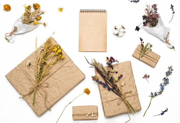 Hediye kutuları sarılı el işi kağıtlar, dekore edilmiş doğal kurumuş çiçekler, boş spiral defter, düz yatak. Sıfır atık tatil hediye paketi. Kadınlar günü, anneler günü ya da paskalya kutlaması konsepti. 