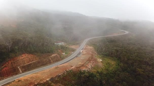 ドローン霧霧の霧の熱帯雨林の近くの曲がりくねった山道の上を飛ぶ 空中からの眺め雄大な熱帯の山々の風景 — ストック動画