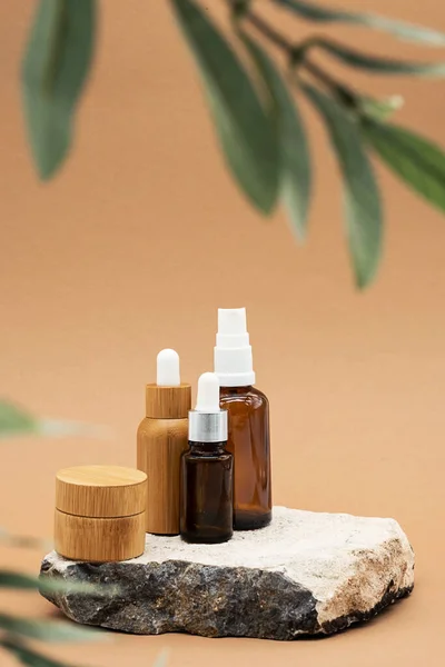 Boş kehribar cam ve bambu esaslı yağ şişeleri, pipette, cam sprey şişesi ve bambu kavanozu doğal taş kürsüde. Organik kaplıca kozmetik güzellik ürünü..