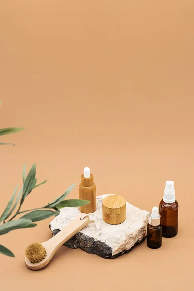 Blank amber glass and bamboo essential oil bottles with pipette, glass spray bottle and bamboo jar on natural stone podium. Organic spa cosmetic beauty product mock up.