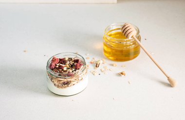 Ev yapımı granola parfe. Hızlı, sağlıklı Yunan yoğurdu, tatlım, kurumuş böğürtlenli granola ve taş masadaki cam kavanozda fındık. Boşluğu kopyala, seçici odak.