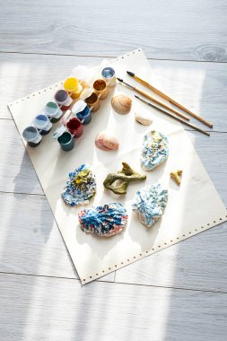 Kabuklu çocuk zanaatı farklı renkler, boya fırçaları ve guaj boyaları ile boyanmış. DIY projesi için deniz kabuğu boyama.