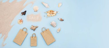 Yaz indirimi konsepti, tanıtım broşürleri. Alışveriş çantalarının yaratıcı yerleşimi, satış - kelime, deniz kabukları ve pastel mavi arka plan üzerindeki kumlar.