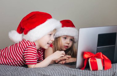 Mutlu bir kız ve bir oğlan bilgisayar ekranına bakıyor, sanal iletişim, tebrikler. Yeni yıl tatili ve çocuklar, sanal iletişim