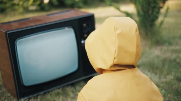 Dítě v bundě se dívá na retro televizi. Na obrazovce zařízení je rušení. — Stock video