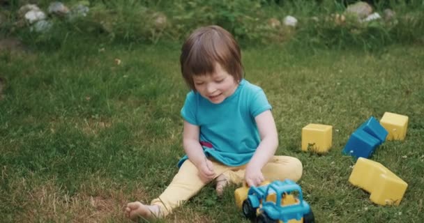 Mała, słodka dziewczyna bawi się zabawkowym samochodem i kostkami na zielonej trawie — Wideo stockowe