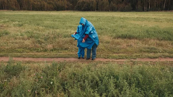 Madre nasconde un bambino piccolo dal vento sotto un impermeabile blu — Foto Stock