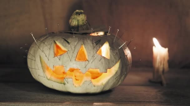 Тыква на Хэллоуин с булавками, застрявшими в ней стоит рядом с горящей свечой — стоковое видео