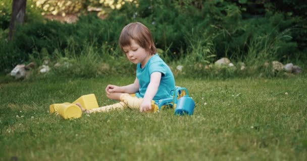 Bonito pequena criança caucasiana brincando na grama verde com um carro de brinquedo — Vídeo de Stock