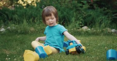 Küçük, sevimli çocuk yeşil çimlerin üzerinde oyuncak araba ve küplerle oynuyor.