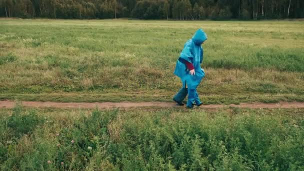 Moeder verbergt een klein kind uit de wind onder een blauwe regenjas — Stockvideo