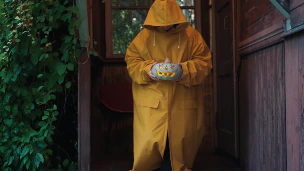 Kobieta w płaszczu przeciwdeszczowym z dynią na Halloween na ganku starego domu — Wideo stockowe