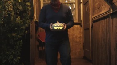 Kovboy şapkalı bir adam eski bir evin verandasında Cadılar Bayramı için balkabağı taşıyor.