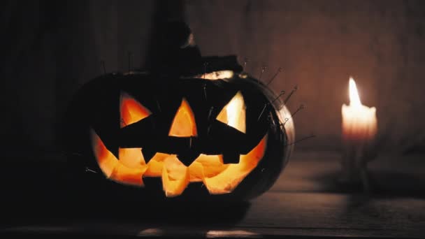 カボチャのハロウィン用ピンがその中に刺さって燃えるキャンドルの隣に立っています — ストック動画