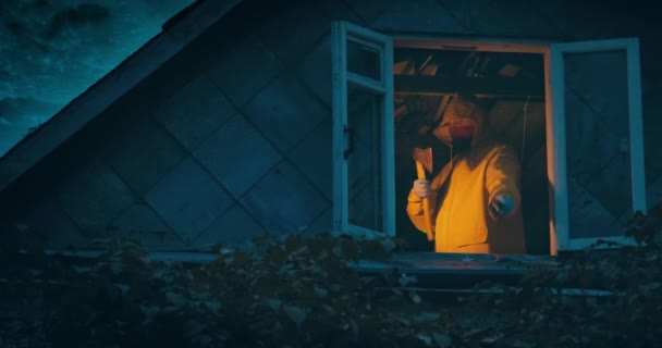 Маніяк в жовтому плащі з сокирою і ножем на верхньому поверсі старого будинку — стокове відео
