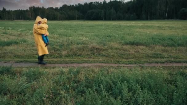 Padre camina en el parque por la noche con un niño pequeño. Gente con impermeables — Vídeo de stock