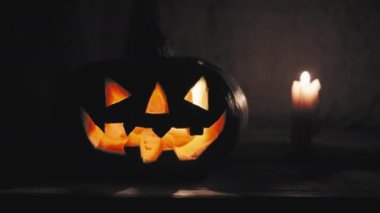 Korkunç yüzlü Cadılar Bayramı balkabağı yanan bir mumun yanında duruyor.