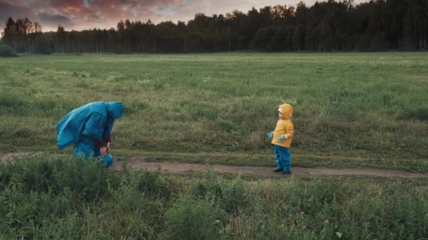 Femeia se joacă cu un copil mic. Apus de soare, vreme tulbure, oameni în paltoane de ploaie — Videoclip de stoc