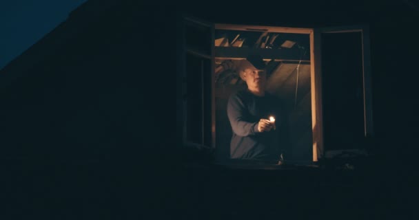 Hombre con sombrero de vaquero en el ático de la casa. Da señal con vela desde la ventana. — Vídeo de stock