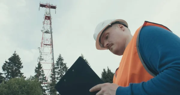 4G 5G baz istasyonu, işçi tulumu ve miğferi yanında duruyor.