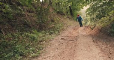 Kırmızı bandanalı bir yürüyüşçü yaz ormanının ortasında dik bir yamaçta yürür.