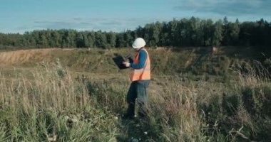 Kum havuzunun yanında beyaz kasklı bir mühendis çalışıyor. Foreman telefonda konuşuyor.