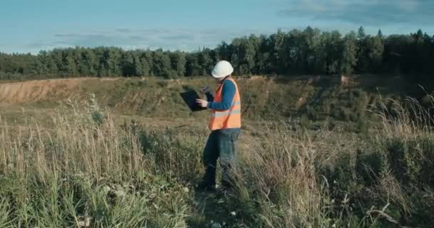 Ingeniero de trabajo en casco blanco junto a una fosa de arena. Foreman está hablando por teléfono. — Vídeos de Stock