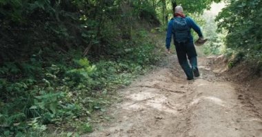 Kovboy şapkalı bir yürüyüşçü yaz ormanının ortasında dik bir yamaçta yürür.