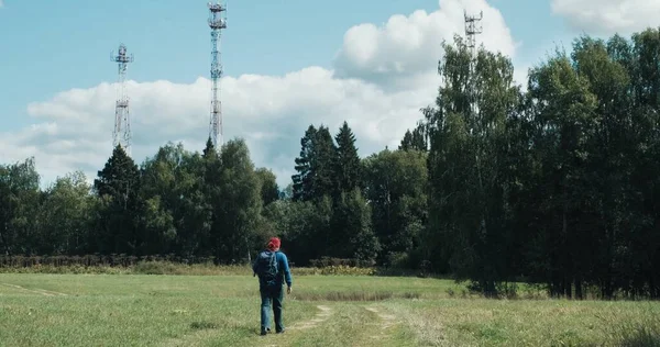 Escursionista con zaino cammina attraverso il campo sullo sfondo delle torri radio 5G — Foto Stock